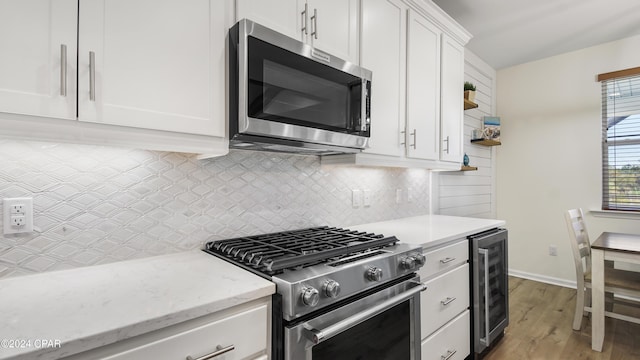 kitchen featuring white cabinetry, light wood-type flooring, stainless steel appliances, beverage cooler, and decorative backsplash