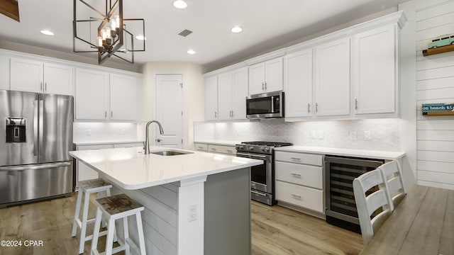 kitchen with an island with sink, sink, white cabinets, wine cooler, and stainless steel appliances