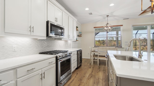 kitchen with sink, appliances with stainless steel finishes, white cabinetry, hanging light fixtures, and tasteful backsplash