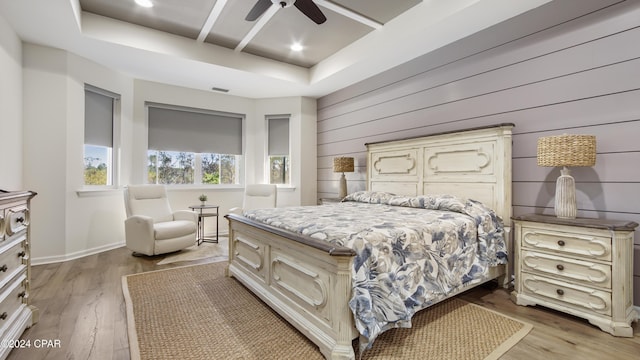 bedroom with a tray ceiling, wood walls, ceiling fan, and light hardwood / wood-style flooring