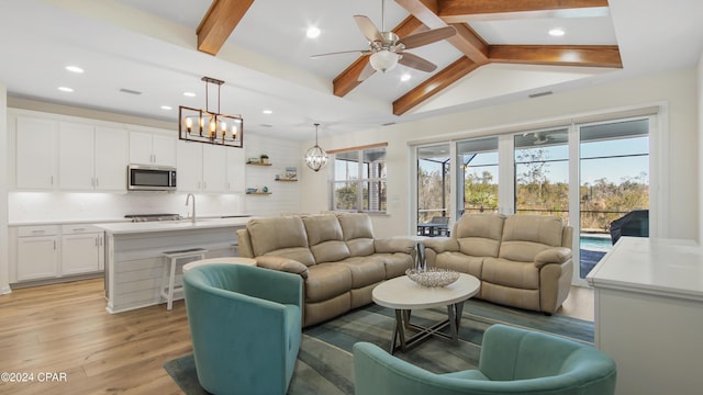 living room featuring ceiling fan with notable chandelier, light hardwood / wood-style floors, and vaulted ceiling with beams