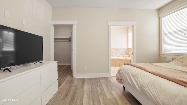 bedroom featuring ensuite bath, a spacious closet, light hardwood / wood-style flooring, and multiple windows