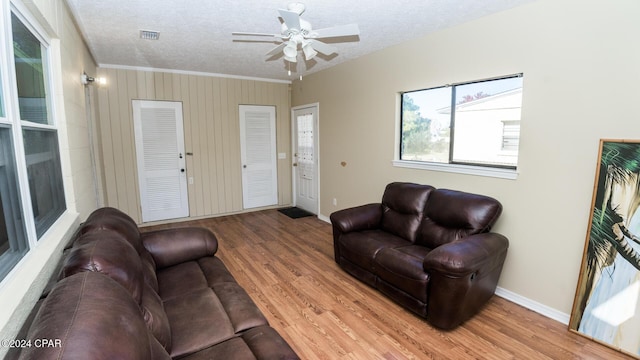 living room with ceiling fan, crown molding, wood-type flooring, and a textured ceiling