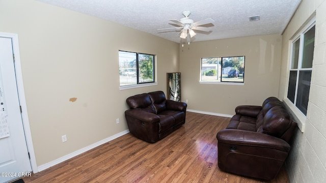 living area with ceiling fan, dark wood-type flooring, and a textured ceiling