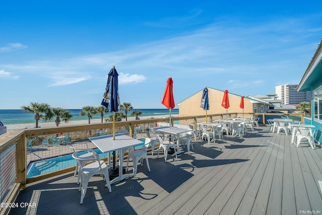 wooden terrace featuring a view of the beach, a water view, and a community pool