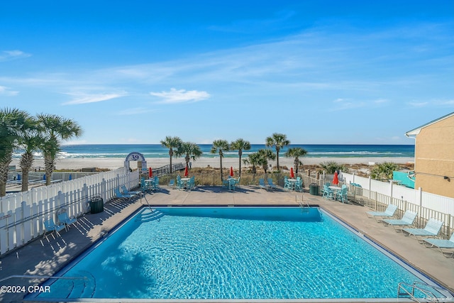 view of swimming pool featuring a water view, a patio, and a view of the beach