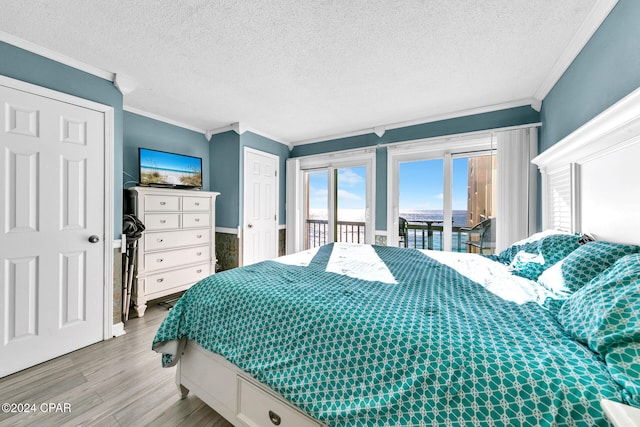 bedroom featuring access to exterior, a textured ceiling, wood finished floors, and ornamental molding