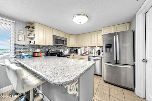 kitchen with stainless steel appliances, cream cabinets, a peninsula, and decorative backsplash