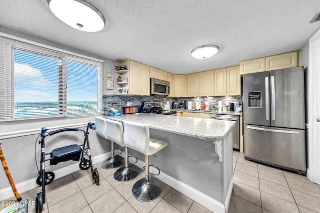 kitchen with a peninsula, light tile patterned floors, cream cabinetry, and appliances with stainless steel finishes