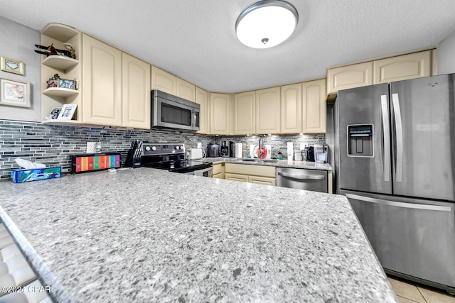 kitchen featuring light tile patterned floors, cream cabinetry, stainless steel appliances, and decorative backsplash