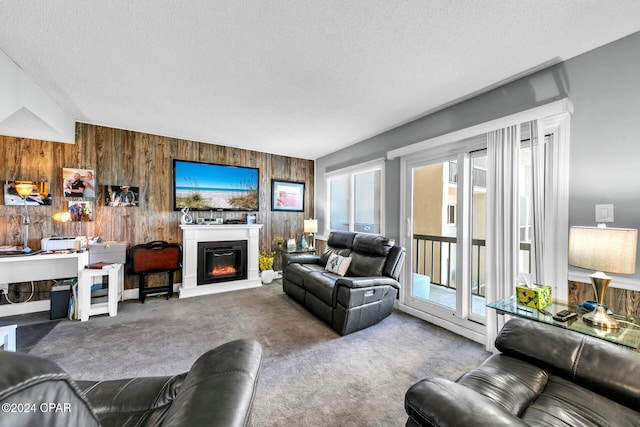 living room featuring carpet flooring, a textured ceiling, wooden walls, and a glass covered fireplace