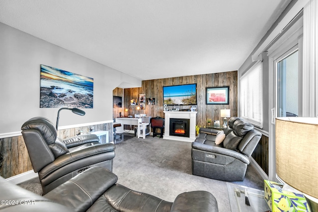 living room featuring a glass covered fireplace, wooden walls, and carpet floors