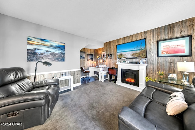 living area with a glass covered fireplace, wooden walls, carpet floors, and a textured ceiling