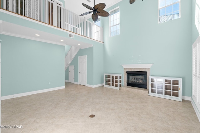 unfurnished living room featuring a tile fireplace, a towering ceiling, a wealth of natural light, and ornamental molding