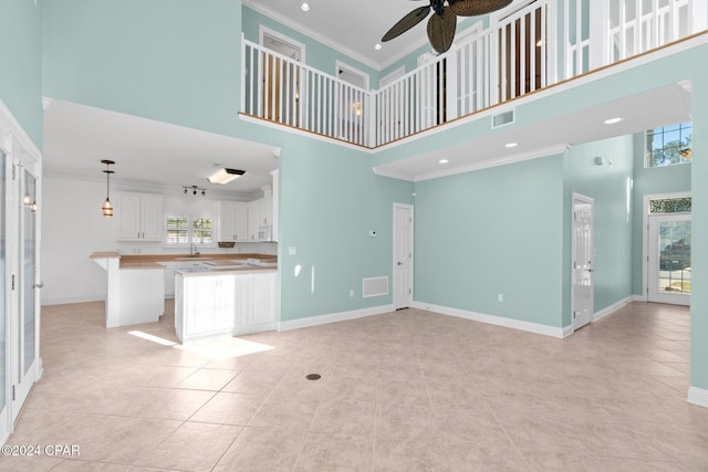 unfurnished living room featuring a healthy amount of sunlight, a towering ceiling, ceiling fan, and crown molding