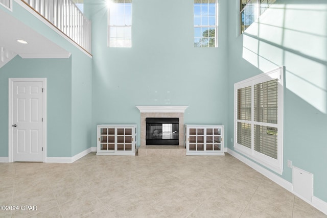 unfurnished living room with a fireplace, a towering ceiling, and light tile patterned flooring