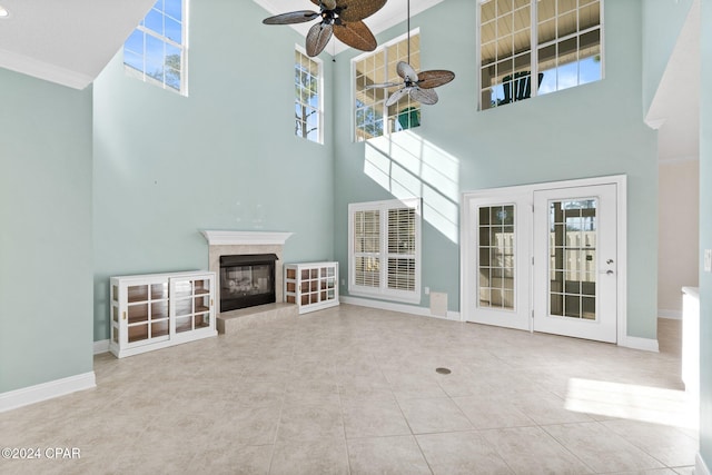 unfurnished living room with a high ceiling, tile patterned floors, ceiling fan, ornamental molding, and a fireplace