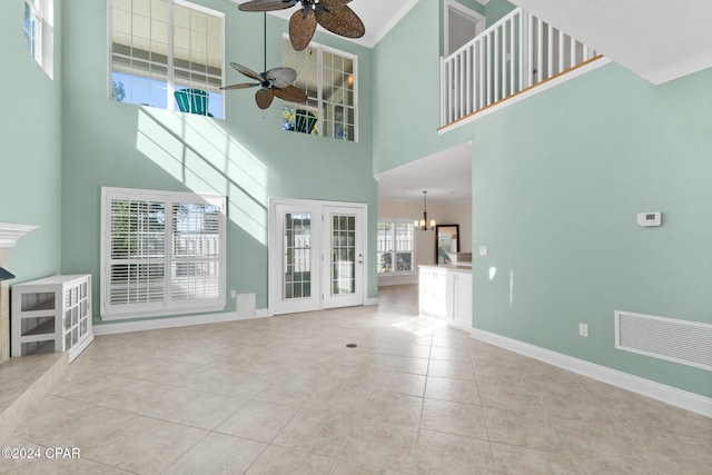 unfurnished living room with light tile patterned floors, a towering ceiling, a healthy amount of sunlight, and ceiling fan with notable chandelier