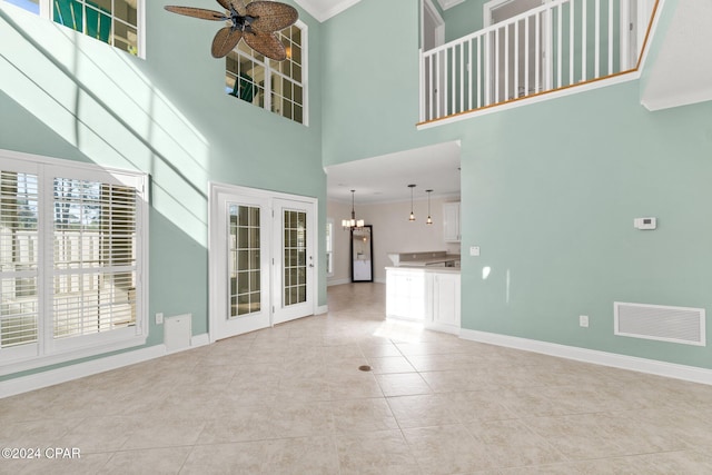 unfurnished living room with ceiling fan with notable chandelier, a towering ceiling, crown molding, and light tile patterned flooring