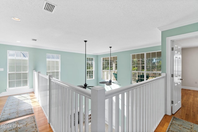 hallway with ornamental molding, a textured ceiling, and light wood-type flooring