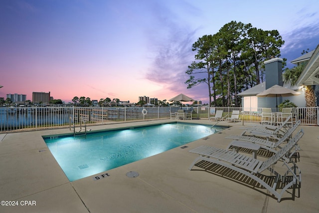 pool at dusk with a patio area and a water view