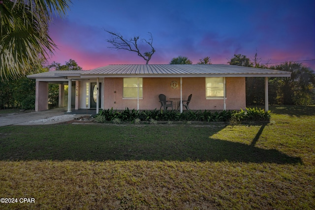 view of front facade with metal roof, stucco siding, concrete driveway, a front lawn, and a carport