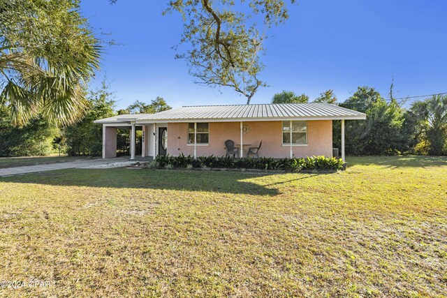 ranch-style house featuring concrete driveway, stucco siding, metal roof, and a front yard