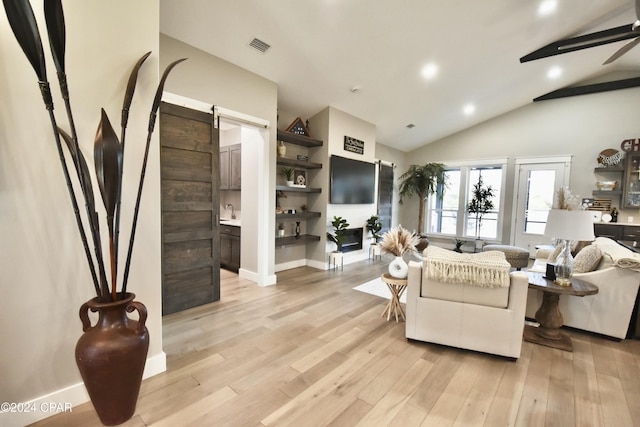 living room featuring ceiling fan, a barn door, light wood-type flooring, and lofted ceiling