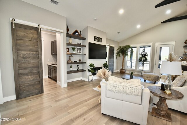 living room featuring light wood-type flooring, a barn door, and vaulted ceiling