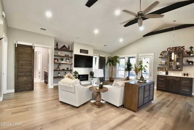 living room with ceiling fan, a barn door, light wood-type flooring, and lofted ceiling