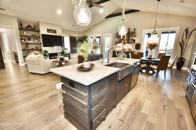 kitchen with light wood-type flooring, light stone counters, sink, a center island with sink, and hanging light fixtures