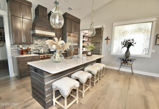 kitchen featuring premium range hood, premium appliances, a kitchen island with sink, sink, and lofted ceiling