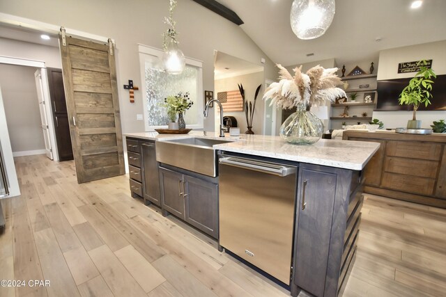 kitchen featuring sink, a barn door, an island with sink, light hardwood / wood-style floors, and decorative light fixtures