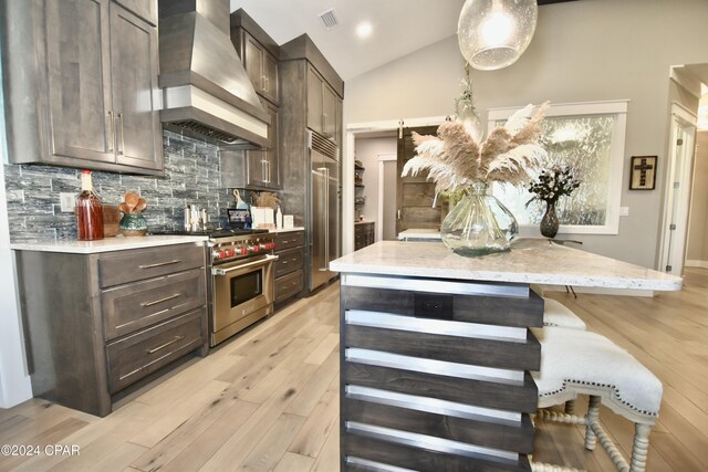 kitchen with wall chimney exhaust hood, premium appliances, tasteful backsplash, pendant lighting, and lofted ceiling