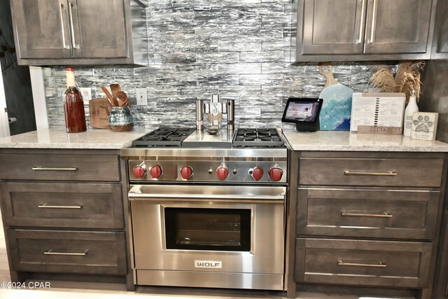 kitchen featuring dark brown cabinetry, decorative backsplash, premium range, and light stone counters