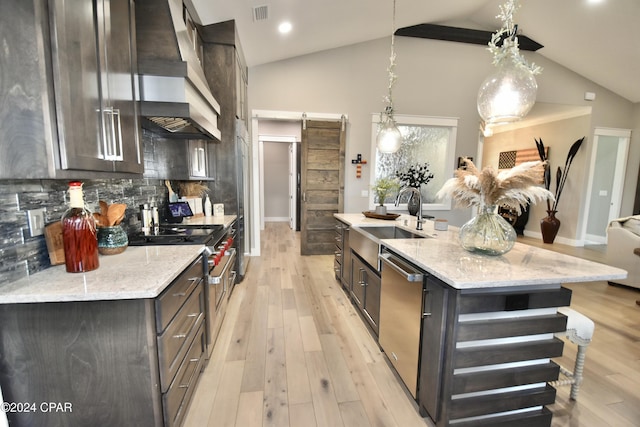 kitchen featuring a barn door, light stone counters, an island with sink, pendant lighting, and appliances with stainless steel finishes