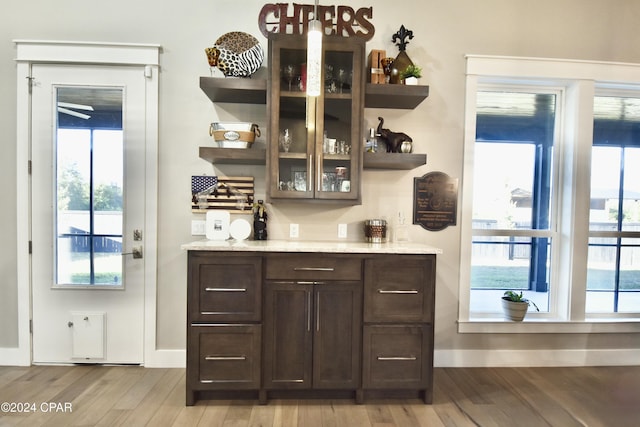 bar featuring light stone counters, dark brown cabinets, hanging light fixtures, and light hardwood / wood-style floors