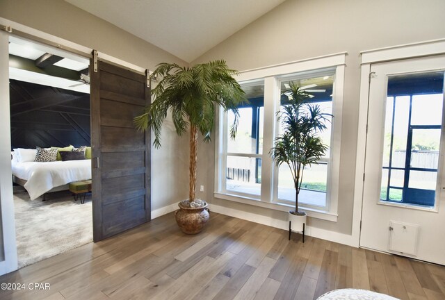 unfurnished bedroom featuring a barn door, wood-type flooring, and vaulted ceiling