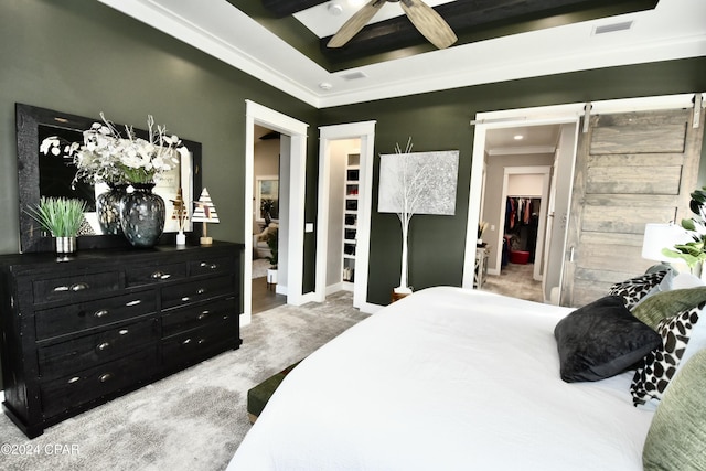 bedroom featuring carpet flooring, ceiling fan, a barn door, a walk in closet, and ornamental molding