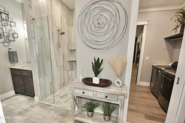 bathroom with tiled shower, hardwood / wood-style floors, vanity, and washing machine and clothes dryer