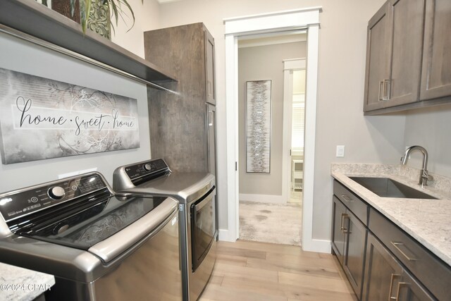 laundry room featuring washing machine and dryer, sink, cabinets, and light hardwood / wood-style flooring