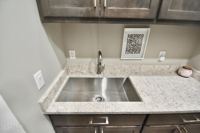 interior details with dark brown cabinetry, light stone counters, and sink