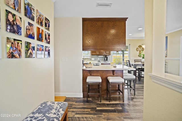 kitchen featuring decorative backsplash, kitchen peninsula, ornamental molding, a breakfast bar, and dark hardwood / wood-style floors