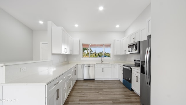 kitchen with white cabinets, sink, appliances with stainless steel finishes, light hardwood / wood-style floors, and kitchen peninsula