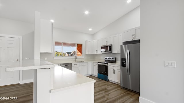 kitchen with white cabinetry, kitchen peninsula, hardwood / wood-style floors, vaulted ceiling, and appliances with stainless steel finishes