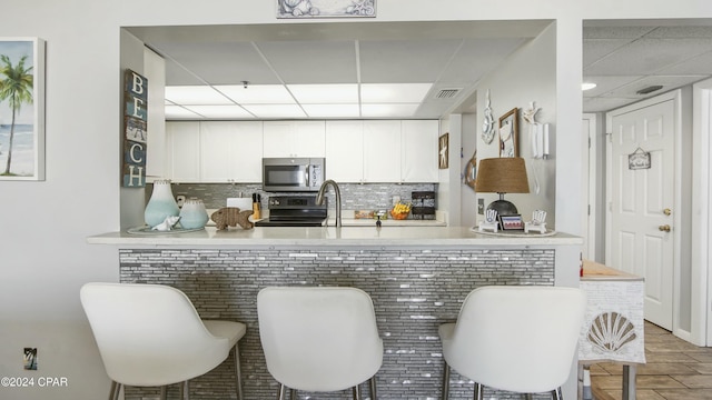 kitchen with white cabinetry, kitchen peninsula, decorative backsplash, and range with electric stovetop