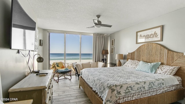 bedroom featuring ceiling fan, a water view, light hardwood / wood-style floors, expansive windows, and a textured ceiling