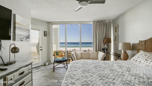 bedroom featuring a view of the beach, access to outside, a textured ceiling, and a water view