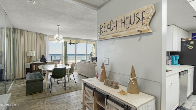 dining area featuring a notable chandelier, floor to ceiling windows, a water view, a textured ceiling, and light hardwood / wood-style flooring