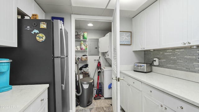 clothes washing area with electric panel and stacked washing maching and dryer